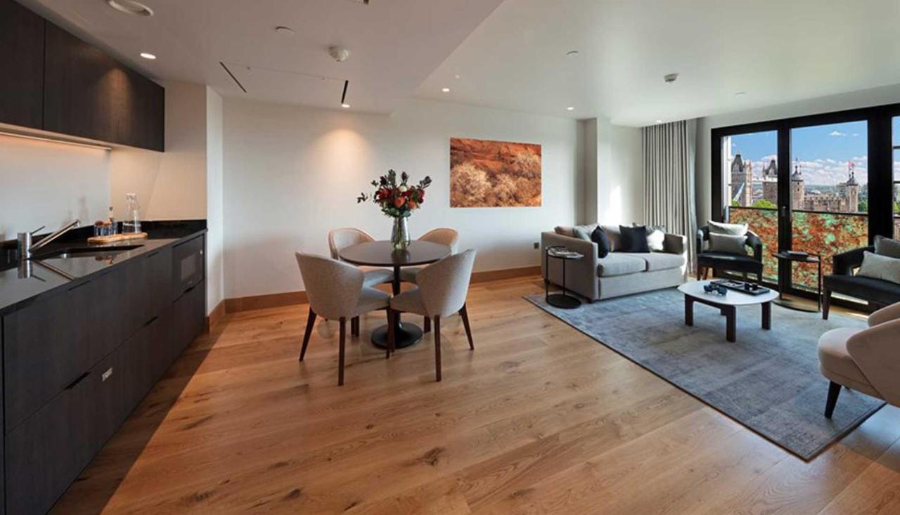 Tower Suites By Blue Orchid London Exteriör bild The photo shows a modern apartment interior. On the left side, there is a kitchen area with dark cabinetry, while on the right side, a comfortable living area is visible. In the center, a round dining table is set with four chairs and a vase of flowe