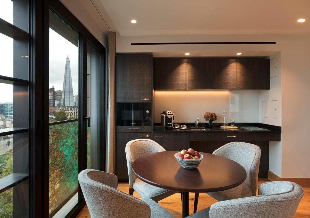 Tower Suites By Blue Orchid London Exteriör bild The photo shows a modern kitchen and dining area. It features a round table with four gray chairs, and a bowl of apples is placed in the center of the table. The kitchen has dark cabinetry, a black countertop, and built-in appliances. Large windows a