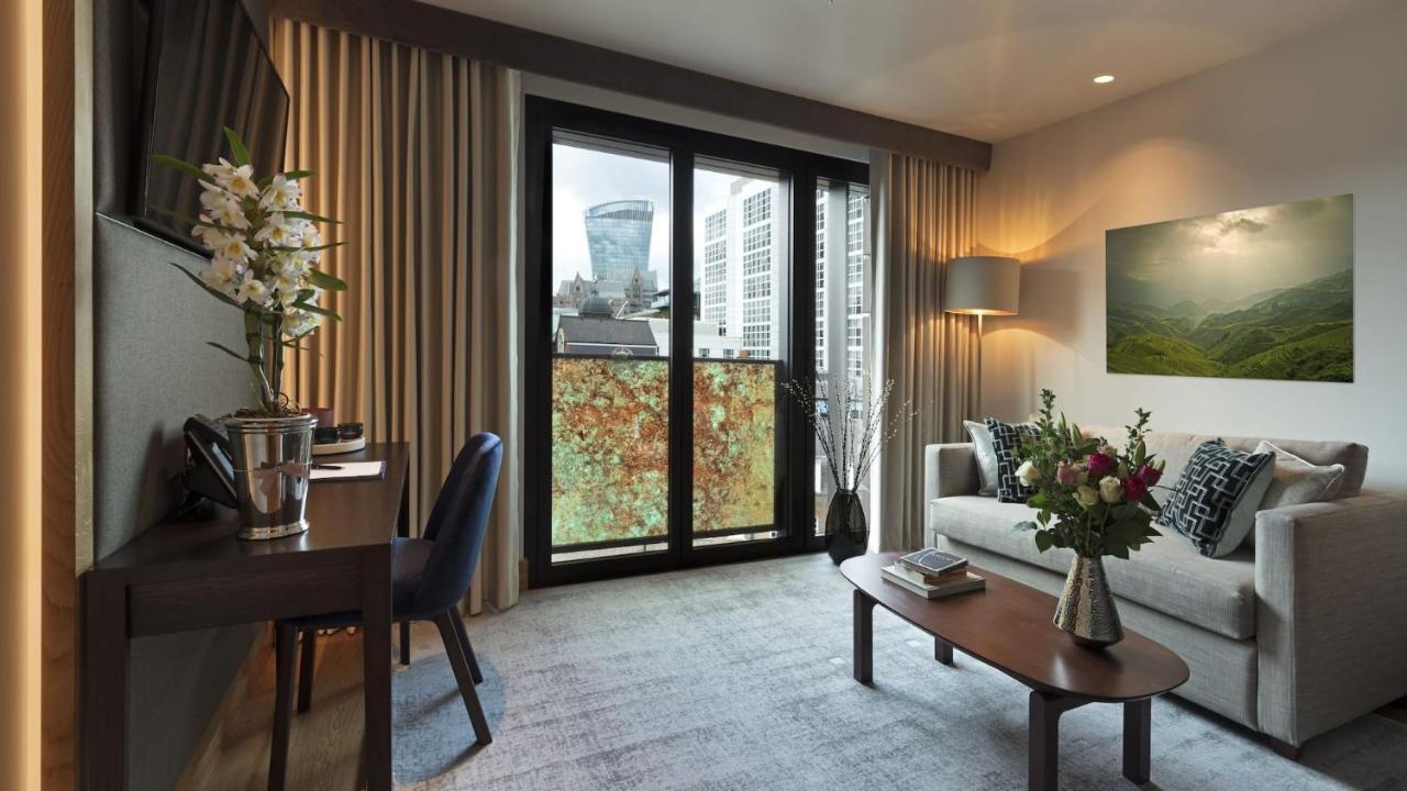 Tower Suites By Blue Orchid London Exteriör bild The photo shows a modern and well-lit living space. There is a comfortable sofa with decorative cushions, a small coffee table in front of it, and a floor lamp providing additional lighting. Beside the sofa, there are decorative plants and a vase wit