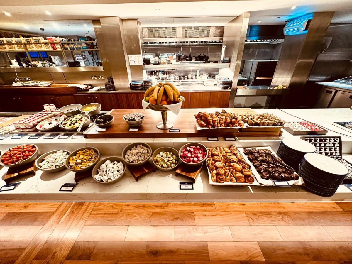 Tower Suites By Blue Orchid London Exteriör bild The photo displays a beautifully arranged buffet featuring a variety of food items. There are several bowls and platters filled with colorful fruits, pastries, and desserts. In the center, a large bowl of bananas is prominently placed. Surrounding th