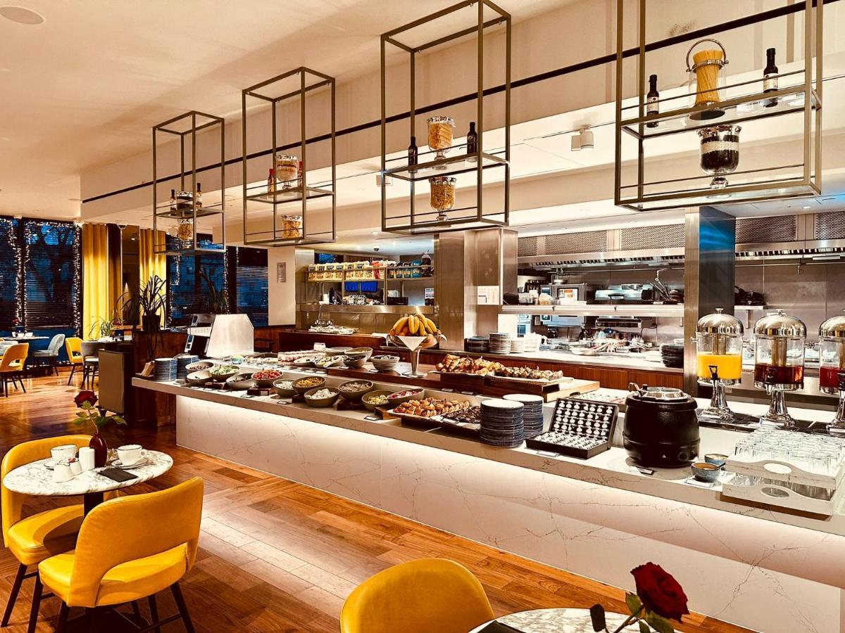 Tower Suites By Blue Orchid London Exteriör bild The photo shows a modern restaurant interior featuring a buffet layout. The space has a sleek design with wooden flooring and a bright, open atmosphere.  

The buffet counter is richly arranged with various dishes and food items, likely for a breakfa