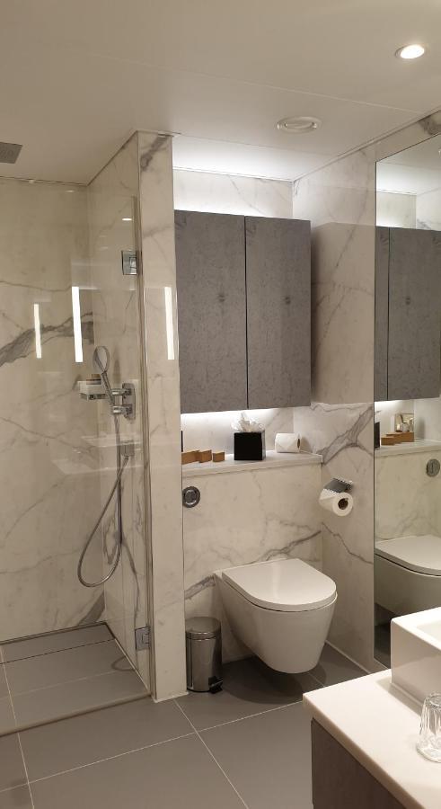 Tower Suites By Blue Orchid London Exteriör bild The photo shows a modern bathroom design featuring elegant marble walls. On one side, there is a transparent shower enclosure with a showerhead and controls visible. Opposite the shower, there is a toilet, and above it are some sleek cabinets. The sp