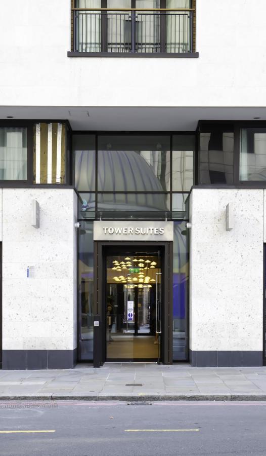 Tower Suites By Blue Orchid London Exteriör bild The photo shows the entrance of a building labeled "TOWER SUITES." The entrance features large glass doors, allowing visibility into the interior. The building has a modern architectural style, with a light-colored stone facade and some decorative el