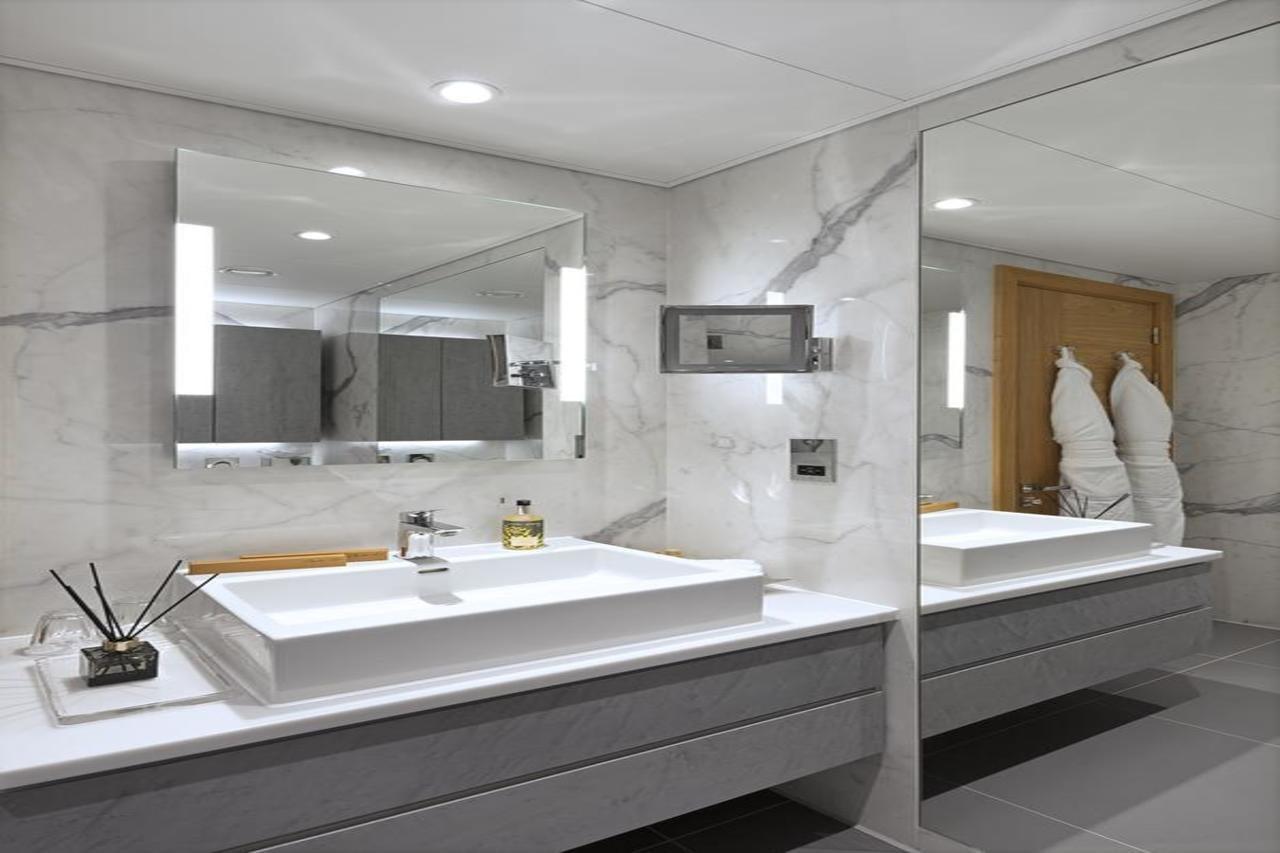 Tower Suites By Blue Orchid London Exteriör bild The photo shows a modern bathroom featuring a sleek design. 

- **Vanity Area**: There is a rectangular sink set into a white countertop, paired with a minimalist faucet. 
- **Mirrors**: Above the sink, there is a large mirror that reflects the entir
